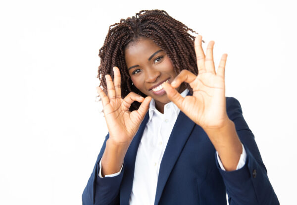 Businesswoman showing ok sign and smiling at camera. Portrait of cheerful young African American businesswoman showing ok sign and looking at camera. Approving concept