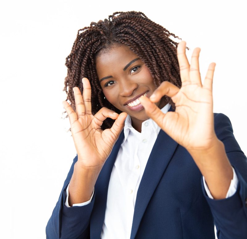 Businesswoman showing ok sign and smiling at camera. Portrait of cheerful young African American businesswoman showing ok sign and looking at camera. Approving concept